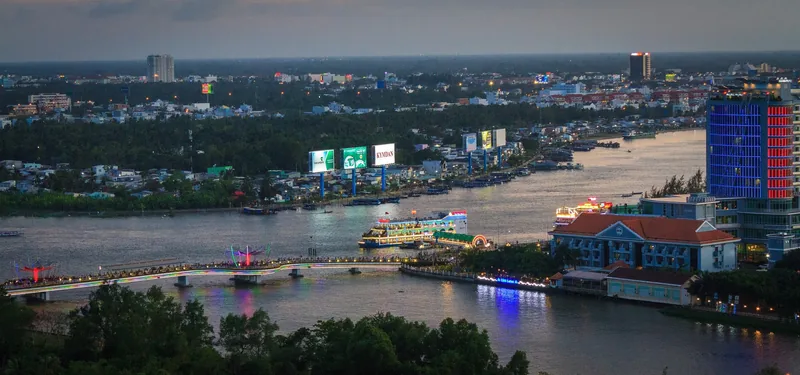 Aerial dusk view of Can Tho city with the river, bridge lights, and riverside buildings glowing at twilight.