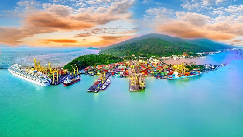 Aerial view of Tien Sa Port in Da Nang with a cruise ship, cargo vessels, and stacked containers by green hills.
