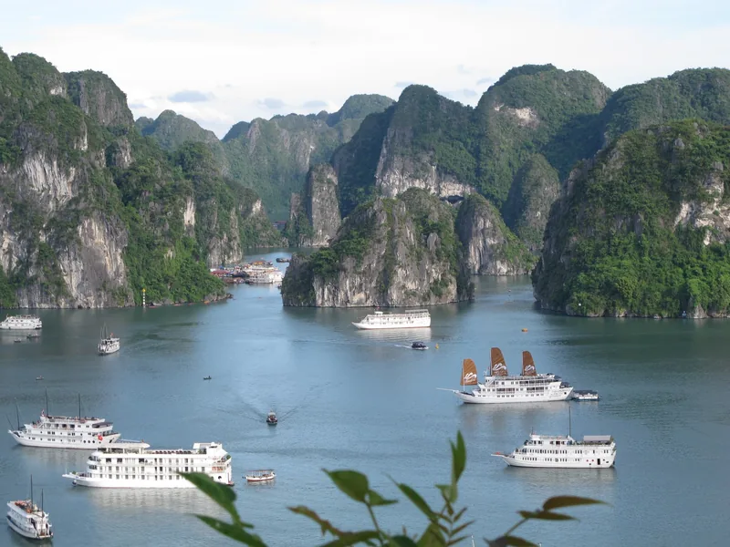 Cruise boats with red sails drift among towering limestone karsts in Ha Long Bay.