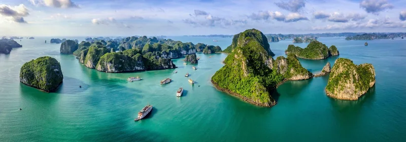 Aerial view of limestone karsts and cruise boats scattered across the turquoise waters of Ha Long Bay