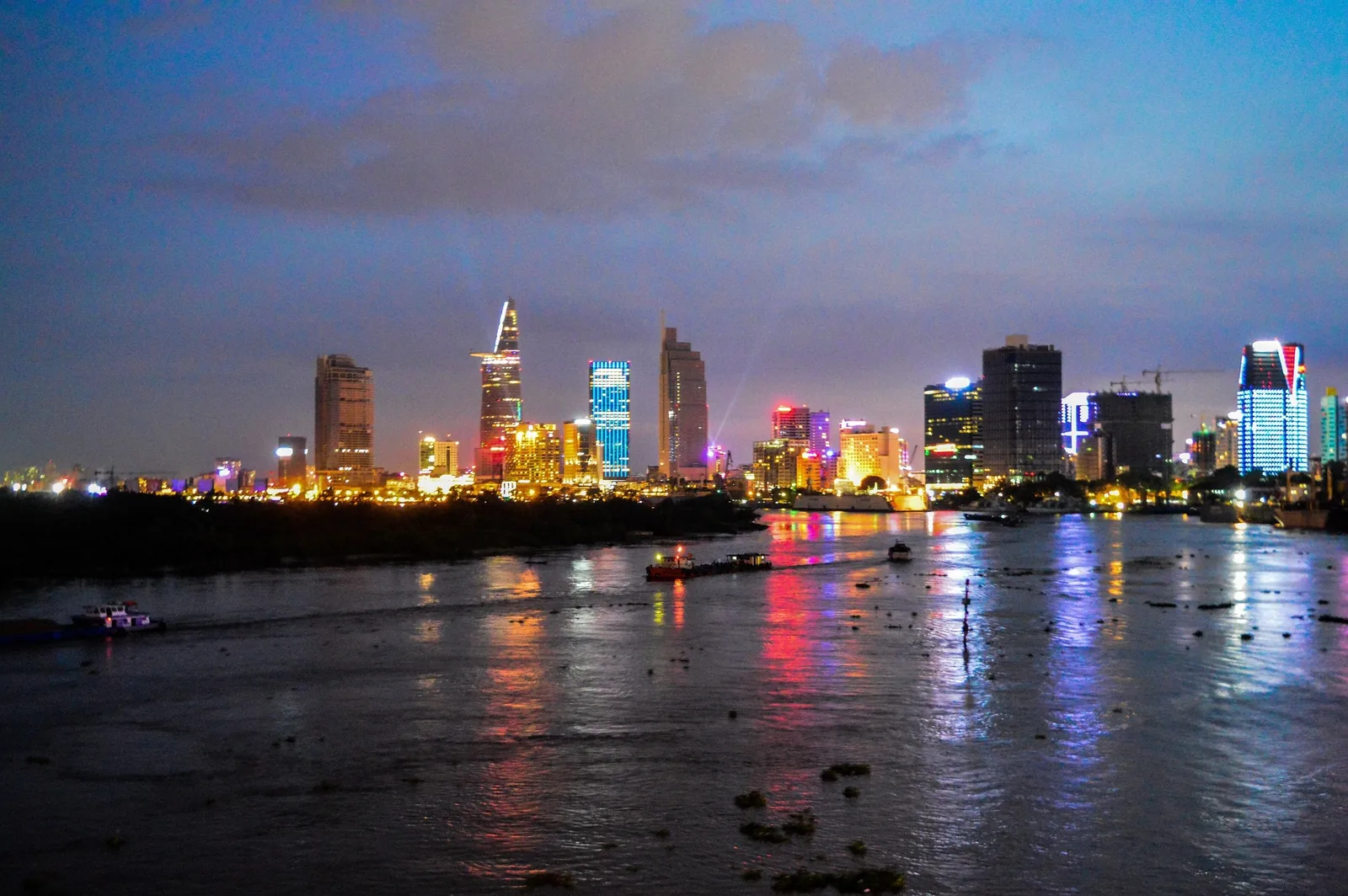 Ho Chi Minh City's illuminated skyline glows above the Saigon River at dusk.