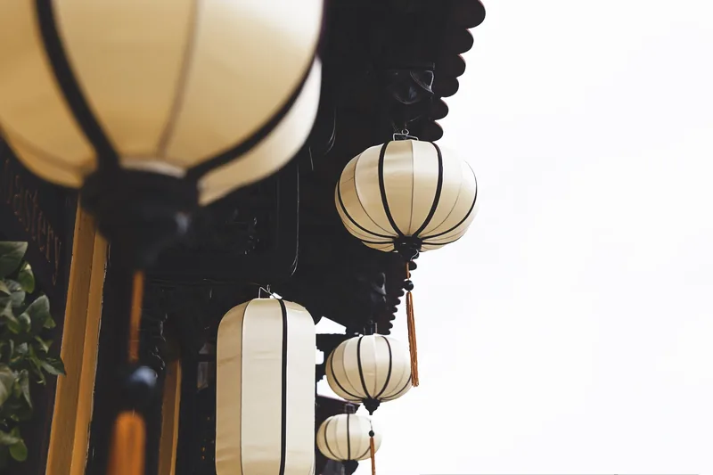 White silk lanterns hang beneath a tiled roof eave in Hoi An's old town.
