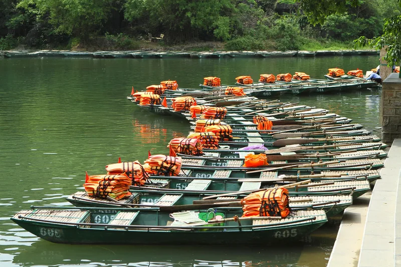Rows of numbered green rowboats with orange life jackets wait at a dock in Trang An, Ninh Binh.