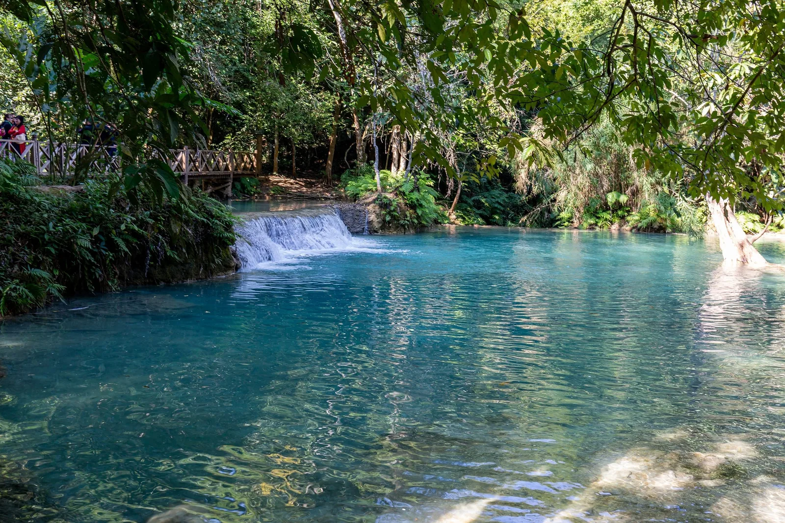 Turquoise pool and small cascade beneath a wooden bridge at Kuang Si Falls near Luang Prabang.