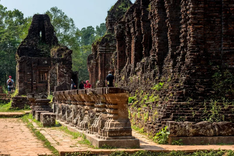 Weathered brick towers and carved balustrades stand among trees at the My Son sanctuary in Vietnam.