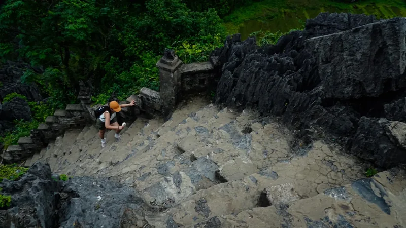 A hiker climbs a steep stone stairway carved into a limestone cliff at Hang Mua in Ninh Binh.