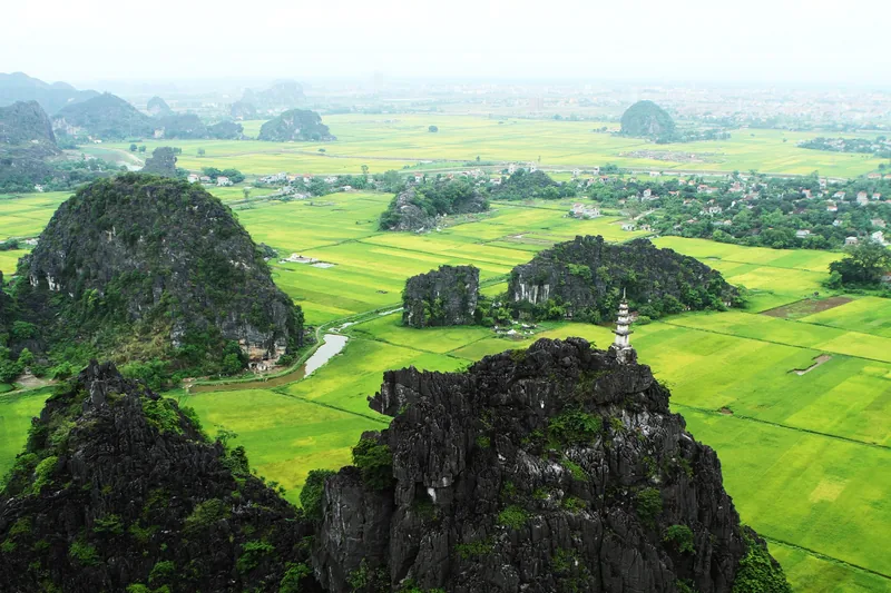 Karst limestone peaks rise above green rice paddies and a winding river near Ninh Binh's Trang An area.